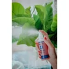 Kép 2/5 - Női kéz kifújja a High Care Simply Red zsírbontó, alakformáló spray-t, zöld, nagylevelű növény előtt