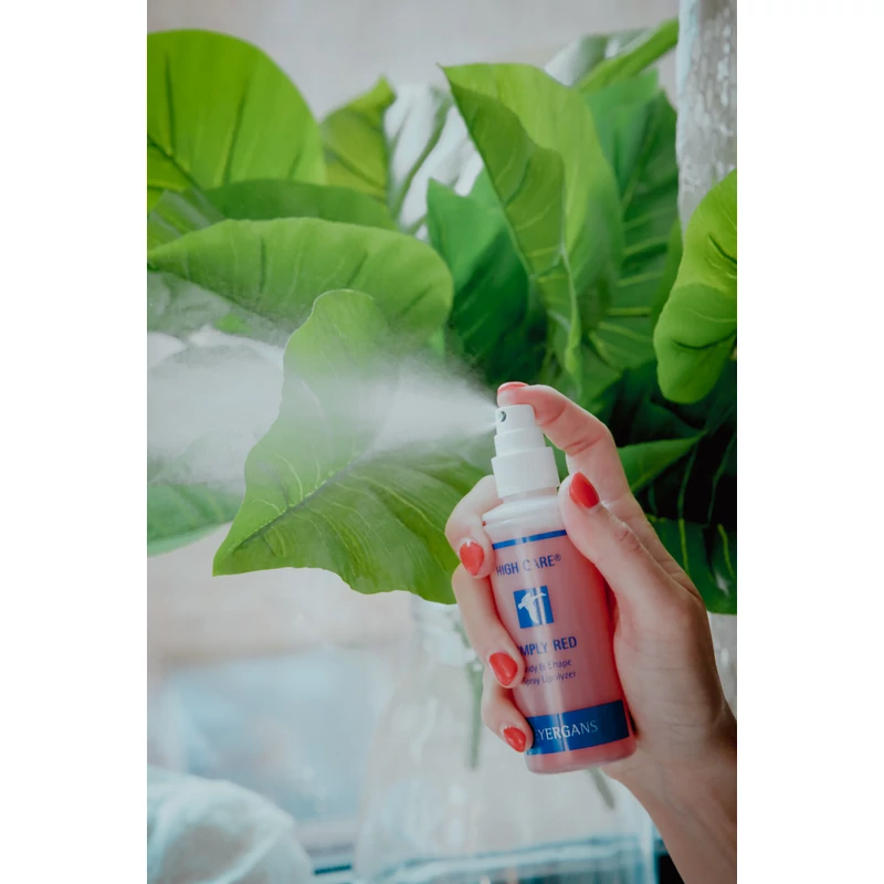 Női kéz kifújja a High Care Simply Red zsírbontó, alakformáló spray-t, zöld, nagylevelű növény előtt